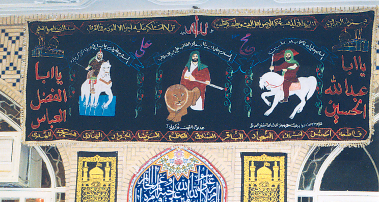 The ceremonial hall in the imamzadeh of Sayyid Muhammad ibn Ali ibn Husayn, decorated with a wall hanging depicting imaginary portraits of Imam Ali, Imam Husayn and Abu al-Fazl al-Abbas. Muharram 2002.