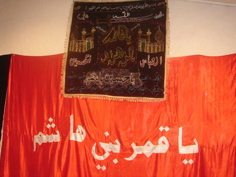 A red flag, alam, from the shrine of al-Abbas in Karbala. On the alam is written ya qamre beni hashem “O, Moon of Hashem’s clan”, a famous al-Abbas epithet. Oslo 2009.