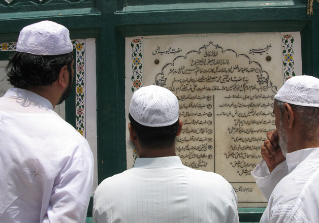 Pilgrims at the Nizamuddin shrine reading a stone inscription showing the spiritual lineage of the saint.
